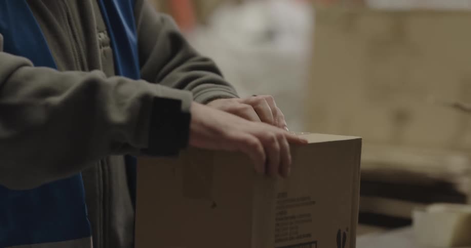 Warehouse worker opening a small cardboard box in the packaging area