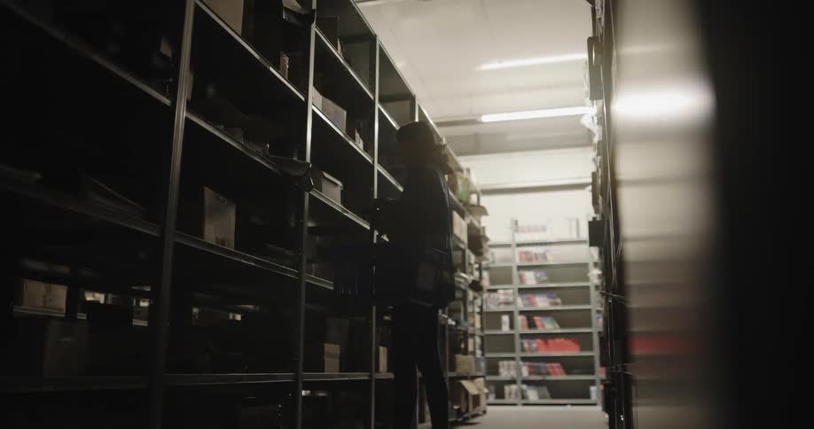A woman with a vest scanning boxes on shelves in a warehouse