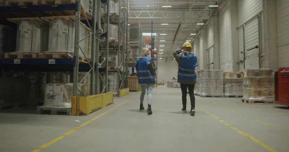 One man and two women with vests walking in a warehouse with shelves