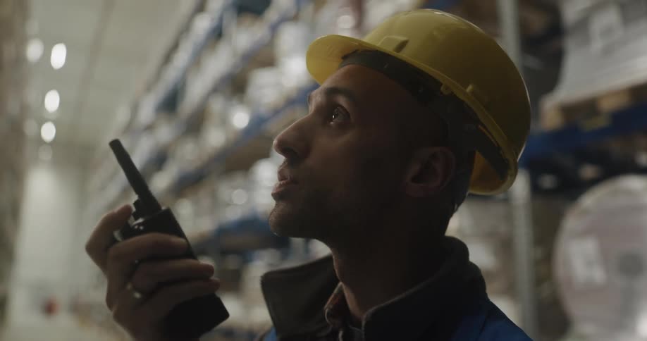 A warehouse employee in a hardhat speaking into a walkie talkie