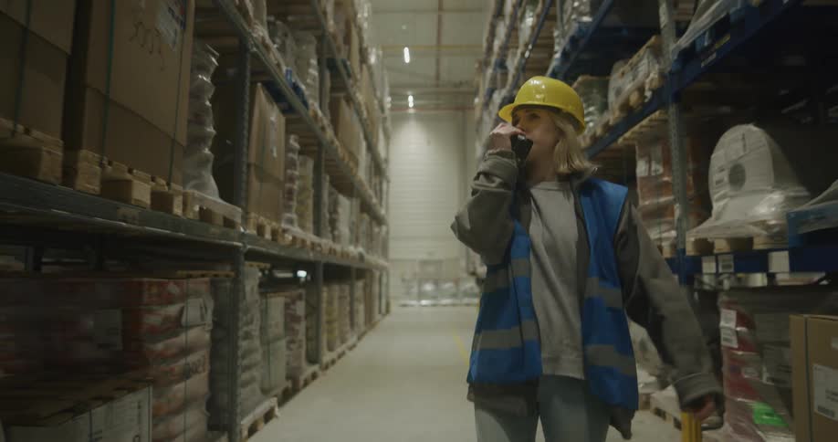 Female warehouse employee walks down aisle talking on two way radio