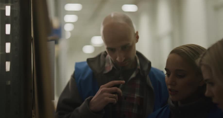 A man with a walkie talkie and two women in a warehouse with lights in the background