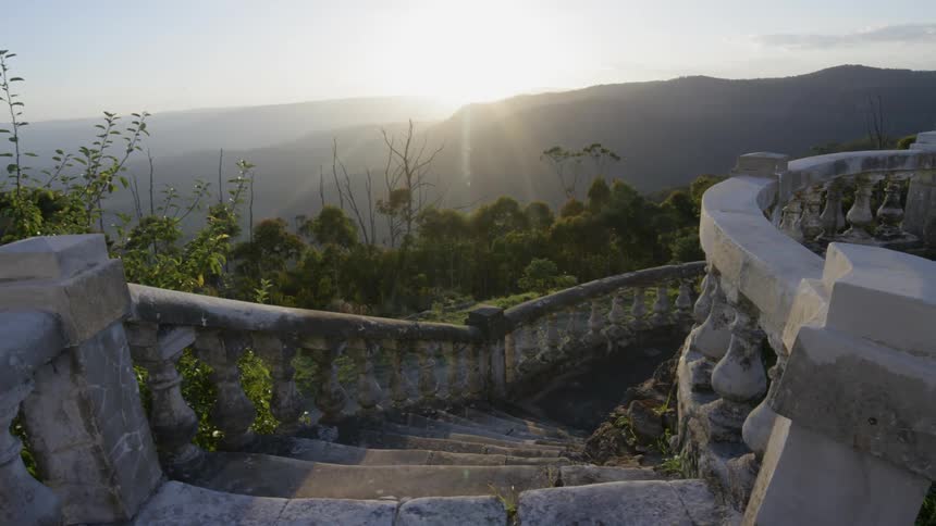 An old stone staircase descends down a slope in bright sunshine