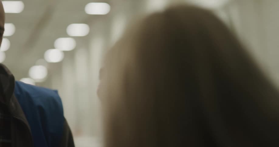 A man and two women with vests in a warehouse with lights in the background