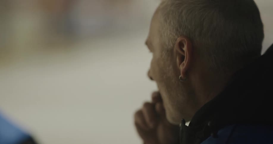 A graying man speaks with another person while eating outdoors during the day
