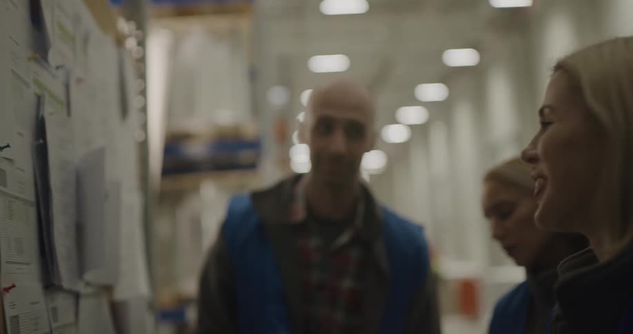 Coworkers talking and laughing while checking information on a billboard in a warehouse
