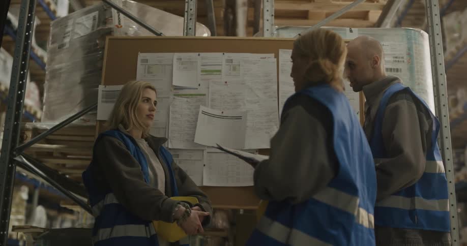 Coworkers talking while checking information on a billboard in a warehouse
