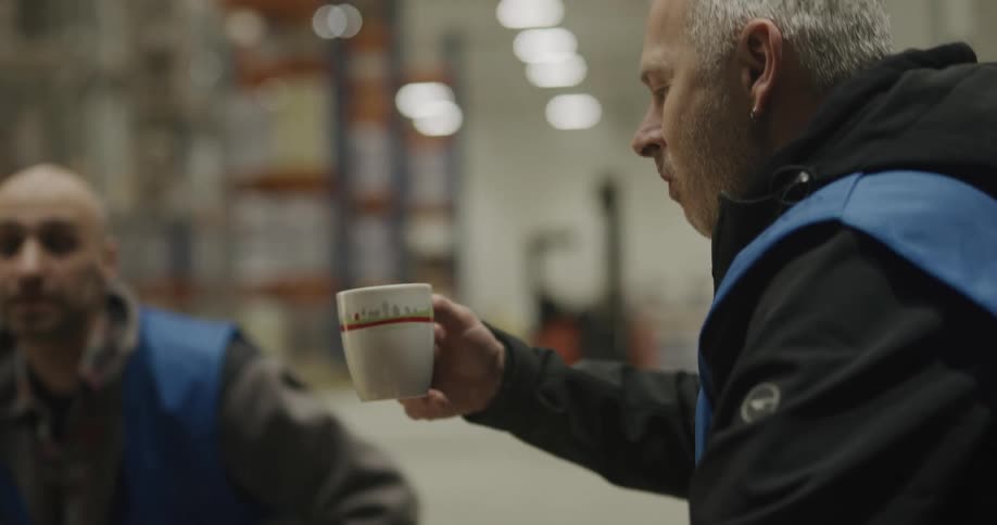A man with a vest in a warehouse drinking coffee from a mug