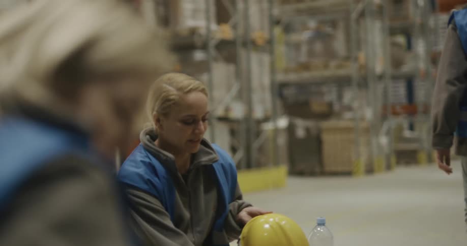 Men and women in a warehouse putting on hardhats with shelves in the background