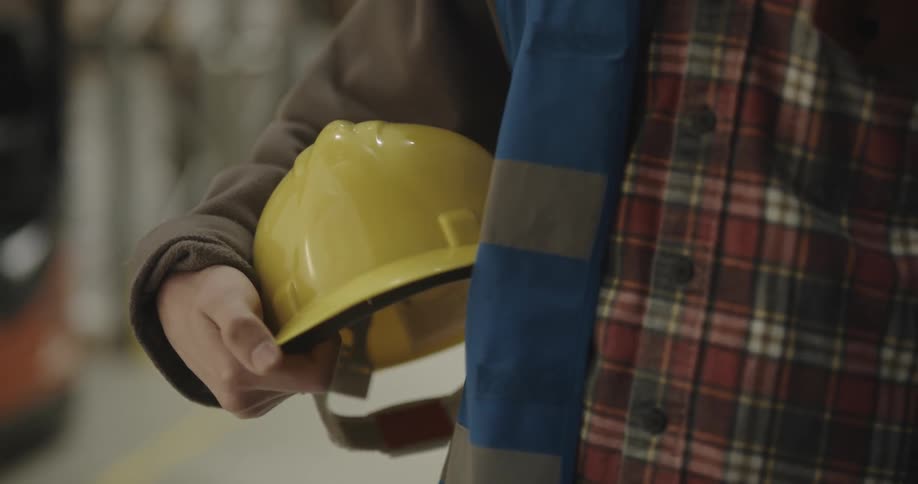 A man stands holding his yellow hardhat while smiling and posing for the camera