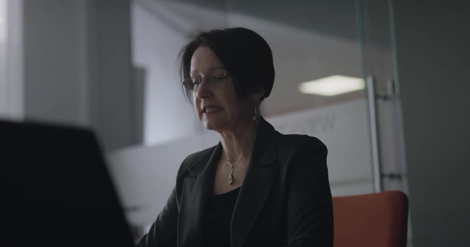 A woman sitting at a desk in a office speaks to someone out of frame