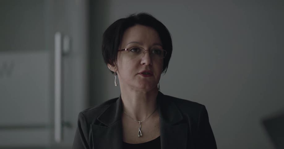 A woman dressed in professional business attire turns her head and looks at people as she speaks