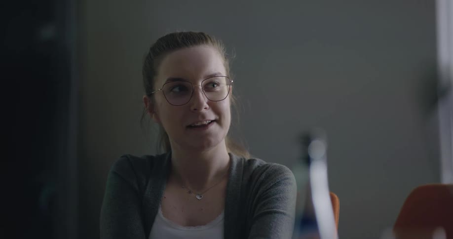 Businesswoman with a ponytail and glasses sitting in chair talks to people in the office