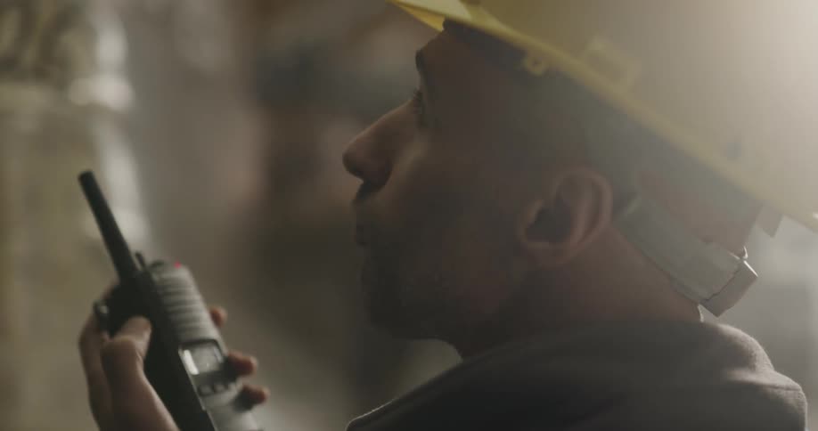 A man with a hardhat and a walkie talkie in a warehouse