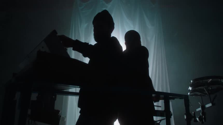 Two silhouetted musicians in a dark room