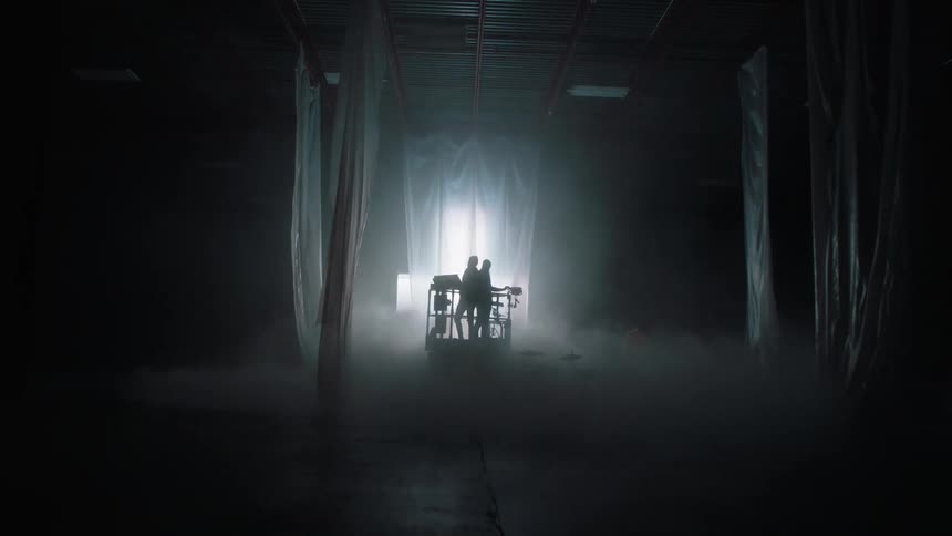 Musicians with instrumets standing inside a lift in front of a digital screen on a smoky room