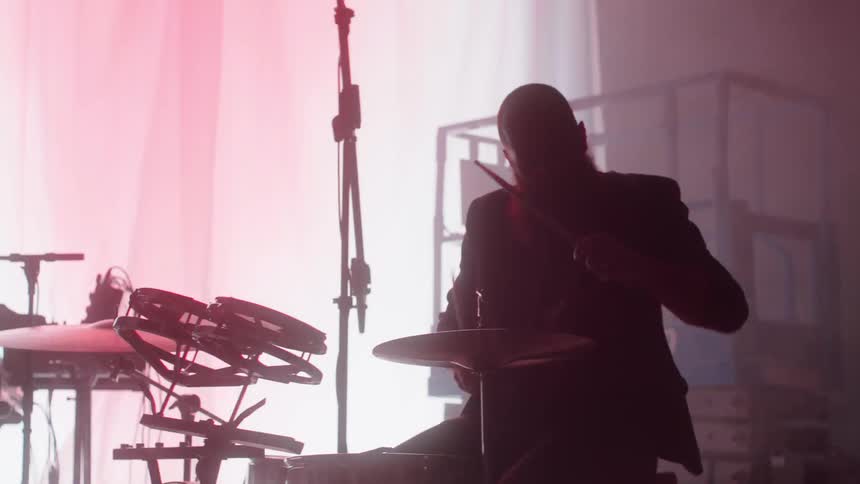 A silhouette of a man on a stage playing the drums with lights flashing