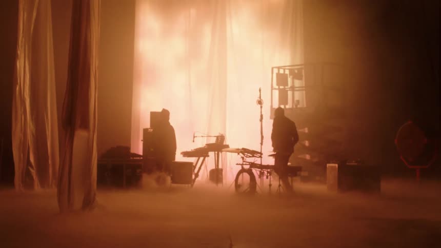 A silhouette of two people on a stage with smoke playing the drums