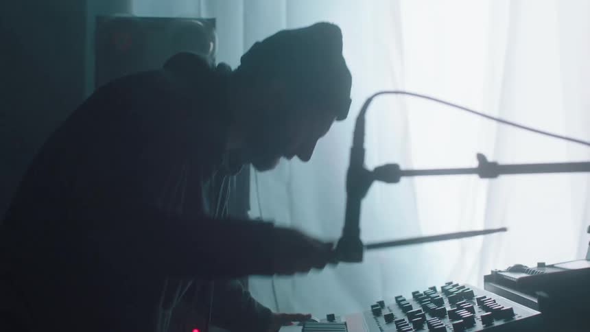 A musician stands over a keyboard and sound mixer while air drumming