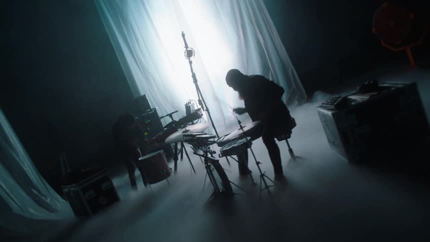 Musicians performing on a stage filled with white smoke in front of strobing lights