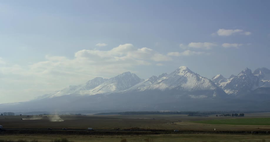 A road through a countryside with a snow capped mountains looming in the distant