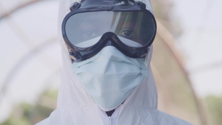 A person with goggles a mask and a hazmat suit with the sky and clouds in the background