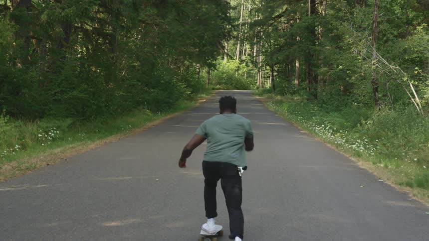 Man riding a skateboard on a rural road through the forest