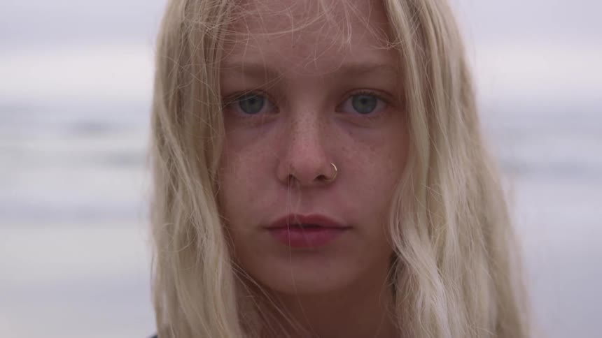 Blonde girl with a nose ring faces the camera with eye contact on the beach