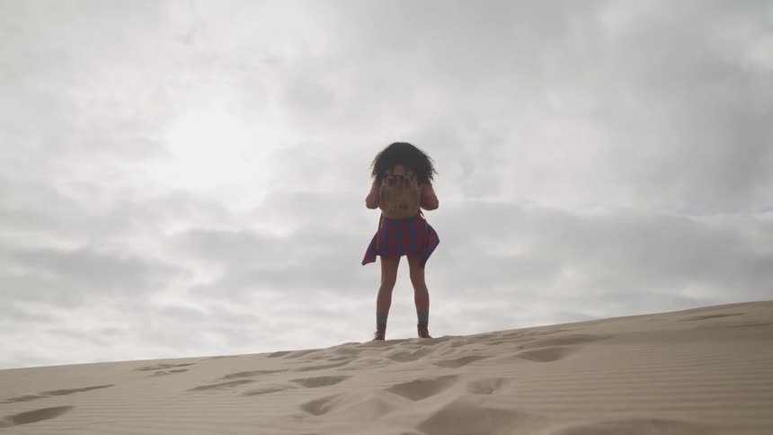 A woman with a backpack standing on sand with the sky and clouds in the background