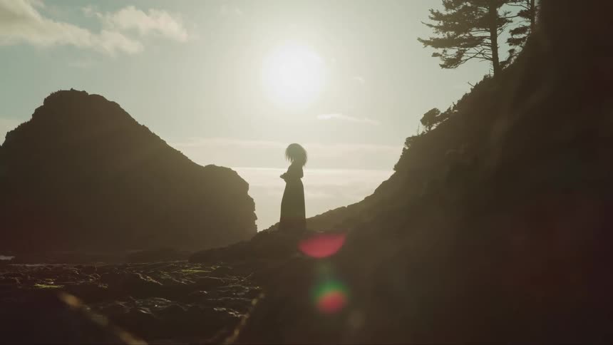 A female standing on a beach looking out at the water