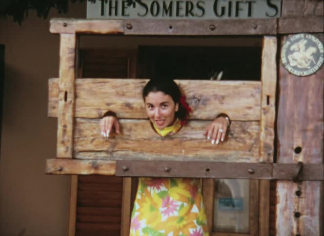 A woman smiles as she poses in a stockade in front of a souvenir shop