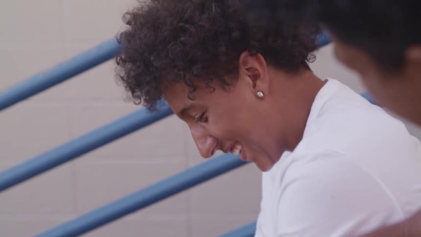 Two boys sitting and talking and laughing on bleachers with a wall in the background
