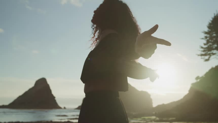 A woman is standing outdoors at dusk and stretching her arms