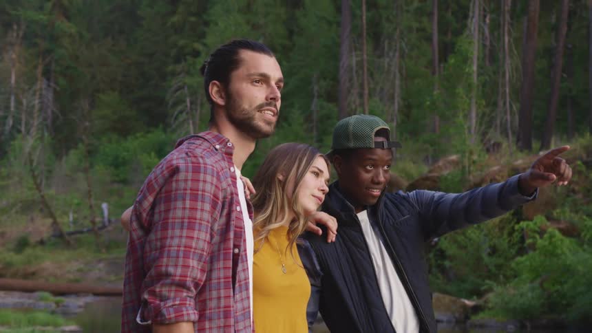 Friends stand with arms around each others shoulders in woods enjoying scene