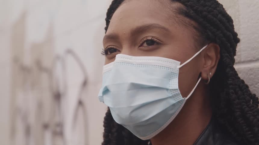 Woman with earrings braids and a mask looks up