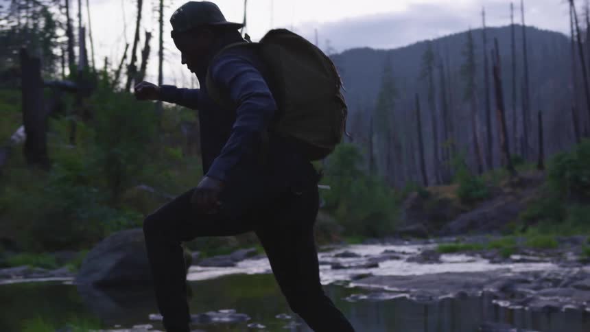 A man runs and jumps across the large stones in a river during the day