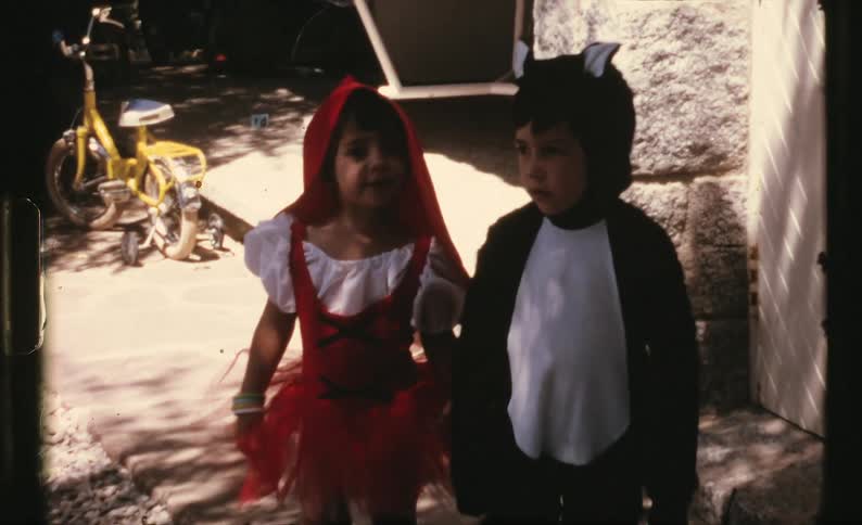 A boy and a girl wearing costumes in a backyard with a bicycle in the background