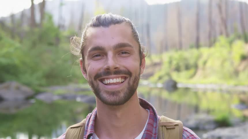 A white male standing in a forest near a river smiling as he looks forward