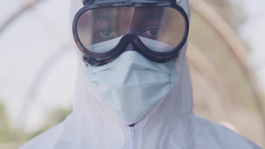A man wearing goggles and a mask and full white ppe suit looks up