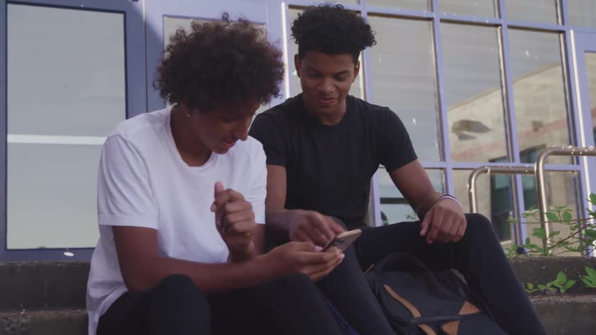 Two friends are sitting on the steps outdoors and talking