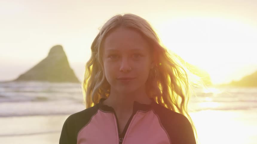A woman opens her eyes and smiles while the wind plays with her blonde hair on the beach