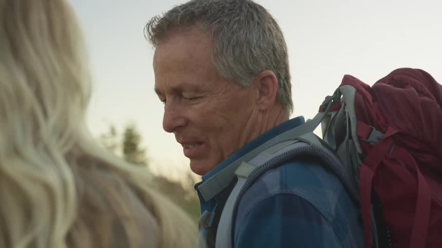 Couple of senior citizen carrying backpacks on the mountain talking at sunset