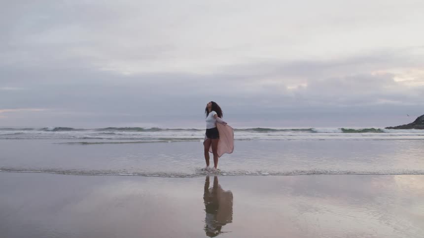 A woman wades in the water and twirls causing her sheer shirt to billow around her