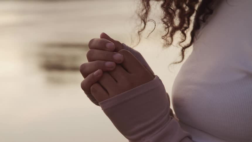 Young woman wearing a long sleeve shirt holding hands in prayer outdoors
