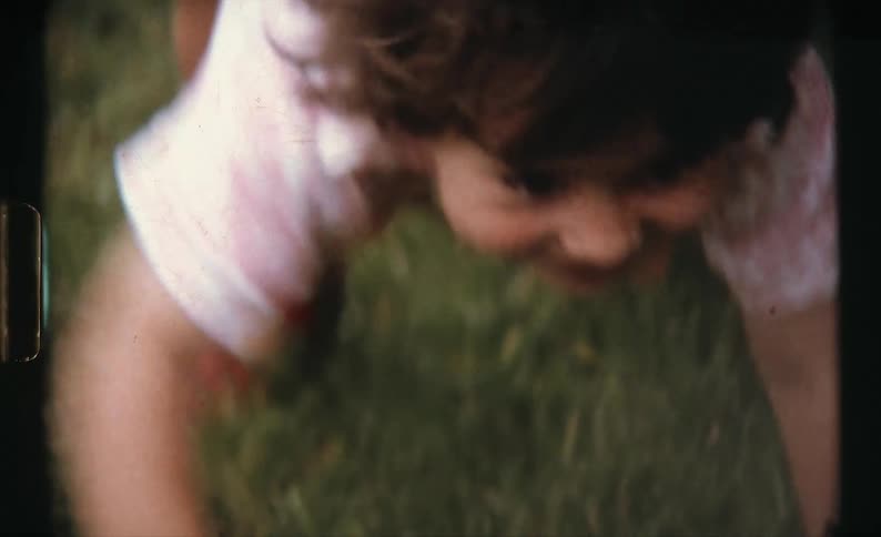 A toddler girl smiling while crawling over a grassy lawn on a summer day