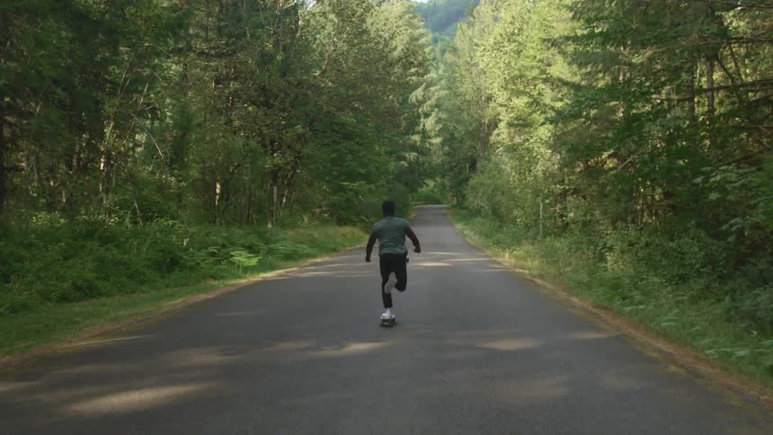 A boy riding a skateboard on a road surrounded by plants and trees