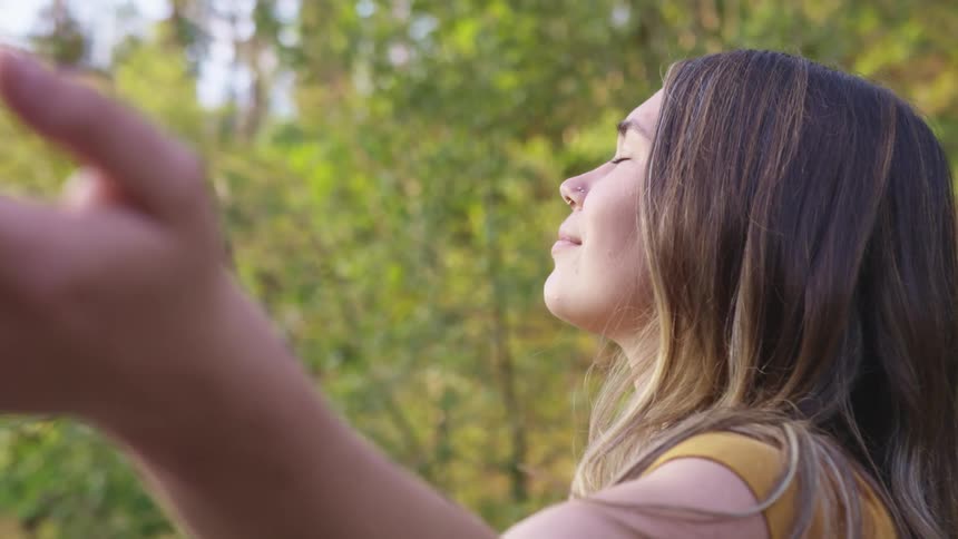 A female standing outside in the woods with her arms out meditating