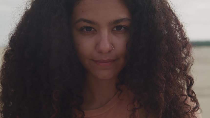 Woman with frizzy hair and nose ring faces the camera with eye contact