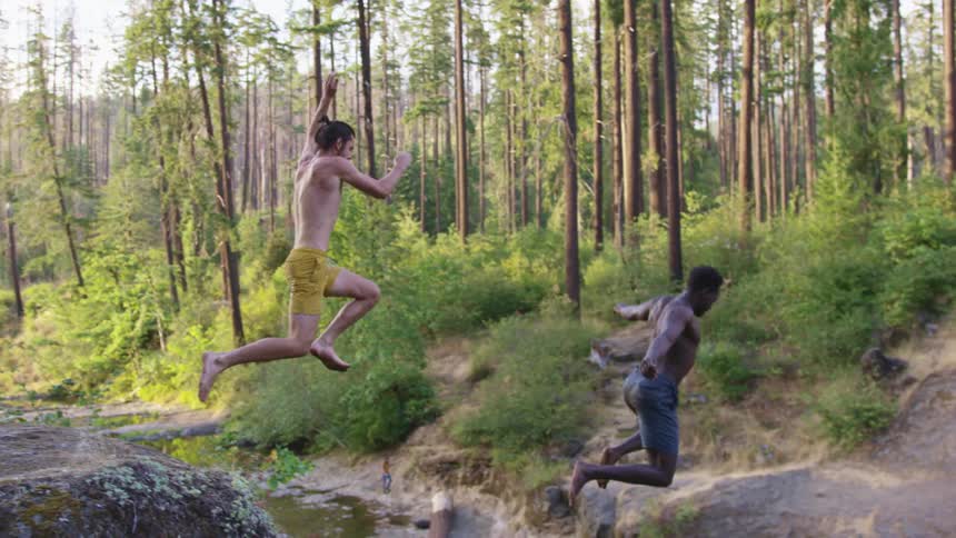 Two men run and jump off the cliff into the stream