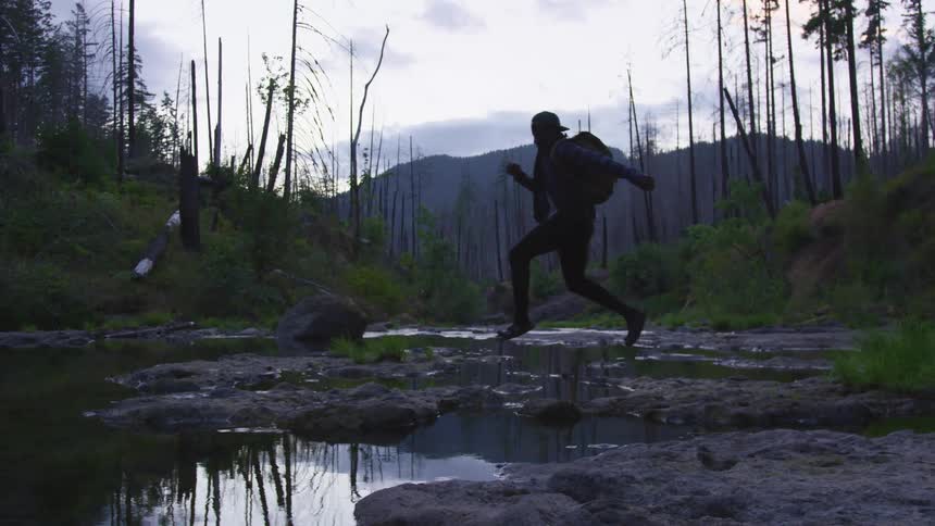 A male running in the woods near a small creek